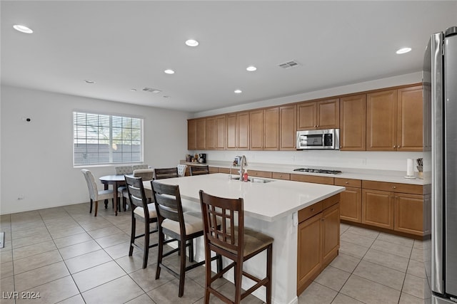 kitchen with an island with sink, sink, a breakfast bar, light tile patterned flooring, and appliances with stainless steel finishes