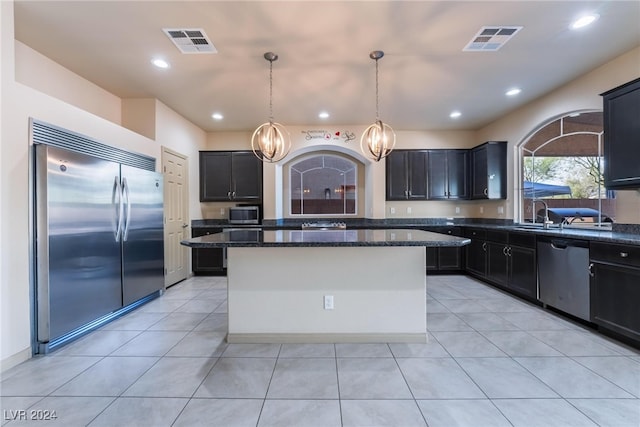 kitchen featuring a kitchen island, dark stone countertops, decorative light fixtures, light tile patterned floors, and appliances with stainless steel finishes