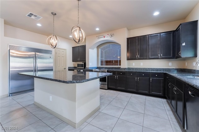 kitchen featuring light tile patterned flooring, a center island, stainless steel appliances, pendant lighting, and dark stone countertops