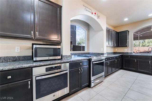 kitchen with appliances with stainless steel finishes, dark stone countertops, a healthy amount of sunlight, and light tile patterned floors