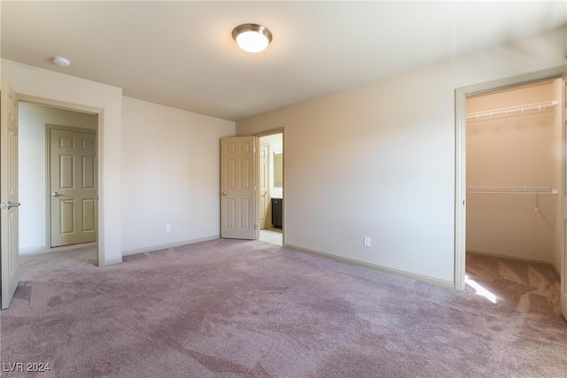 unfurnished bedroom featuring a spacious closet, light carpet, and a closet