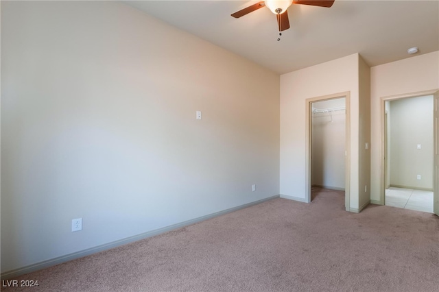 unfurnished bedroom featuring a spacious closet, light carpet, a closet, and ceiling fan