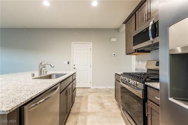 kitchen with a center island with sink, sink, dark brown cabinetry, appliances with stainless steel finishes, and light stone counters