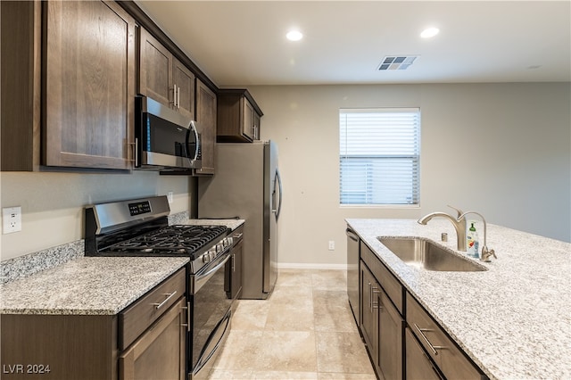 kitchen featuring appliances with stainless steel finishes, light stone countertops, sink, and dark brown cabinets