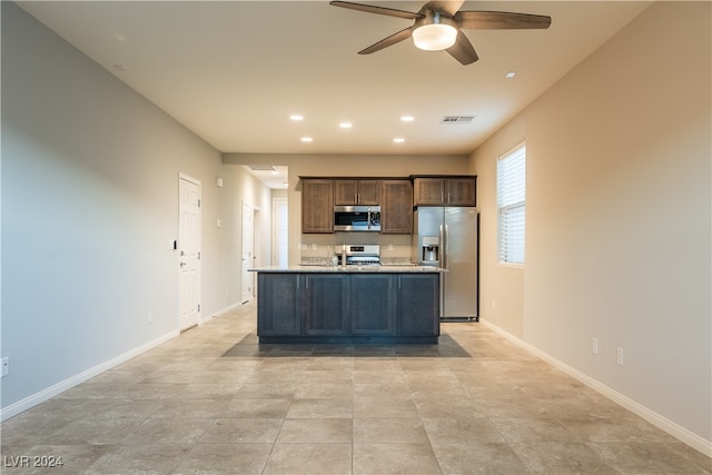 kitchen featuring ceiling fan, stainless steel appliances, dark brown cabinetry, and an island with sink