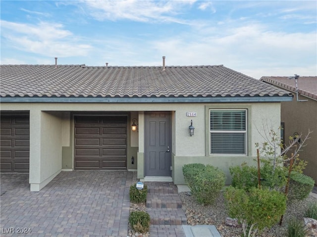 2664 Chinaberry Hill St, Laughlin, NV 89029 - view of front facade featuring stucco siding, an attached garage, a tile roof, and decorative driveway