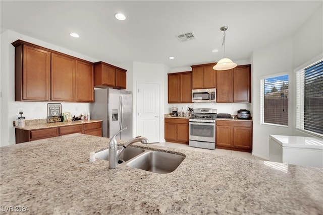 kitchen featuring light stone countertops, stainless steel appliances, sink, and pendant lighting