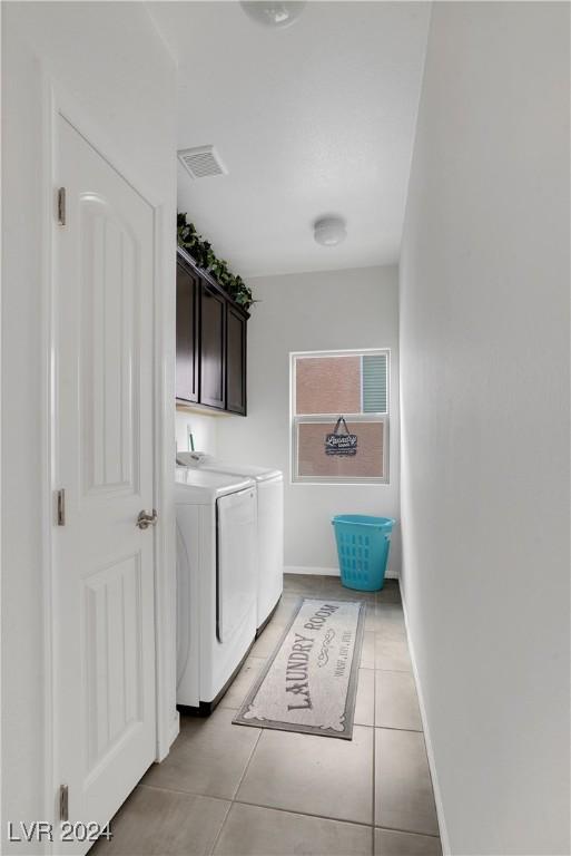 washroom with washing machine and dryer, light tile patterned floors, and cabinets