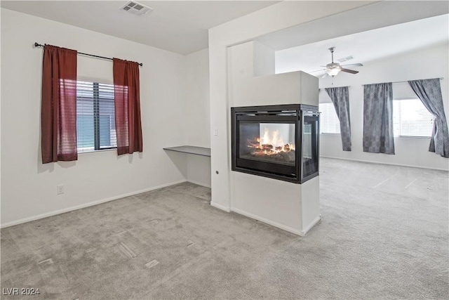 unfurnished living room featuring ceiling fan, a multi sided fireplace, and light colored carpet