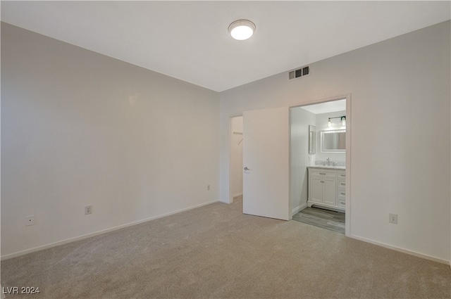 unfurnished bedroom with a walk in closet, sink, light carpet, and ensuite bath