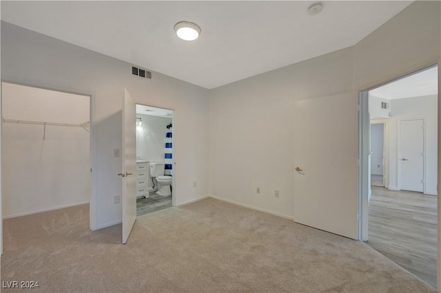 unfurnished bedroom with a closet, visible vents, a walk in closet, and carpet