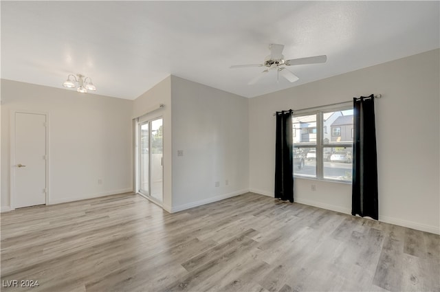 spare room featuring ceiling fan with notable chandelier and light wood-type flooring