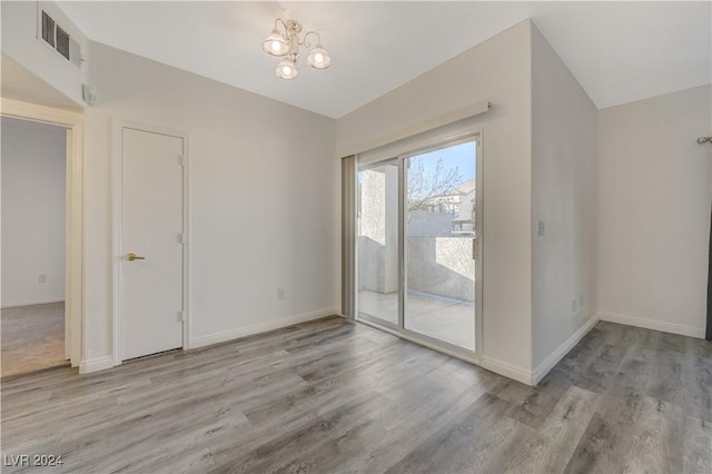 unfurnished room featuring baseboards, visible vents, a chandelier, and wood finished floors