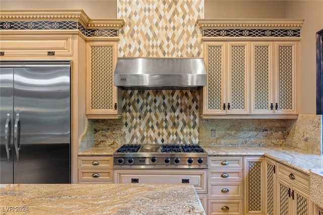 kitchen featuring decorative backsplash, light stone countertops, wall chimney range hood, and appliances with stainless steel finishes