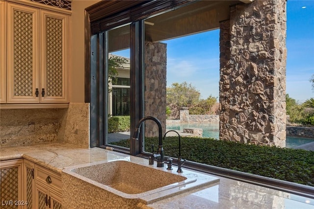 kitchen with backsplash, light stone counters, and sink