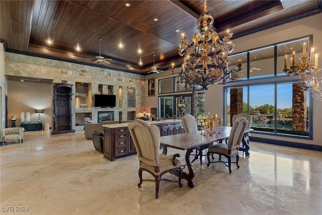 dining area with a tray ceiling, a large fireplace, a high ceiling, and ceiling fan with notable chandelier