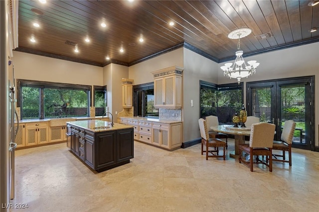 kitchen with light stone countertops, sink, decorative light fixtures, a kitchen island with sink, and dark brown cabinets