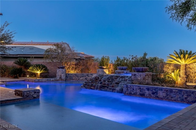 pool at dusk with a jacuzzi and pool water feature