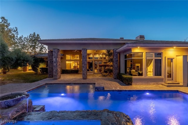 pool at dusk featuring ceiling fan and a patio area