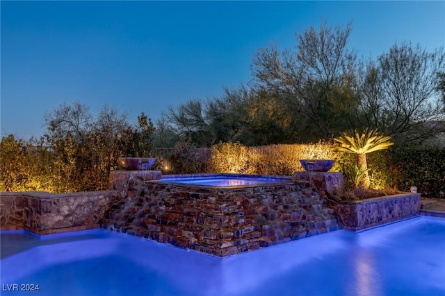 pool at dusk featuring a hot tub