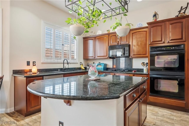 kitchen with a kitchen island, a sink, light wood-style floors, dark stone counters, and black appliances