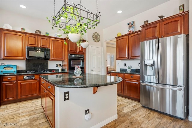 kitchen featuring black microwave, light wood-style floors, stainless steel fridge with ice dispenser, a center island, and dark stone counters