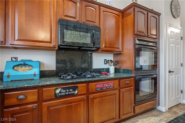 kitchen featuring dark stone counters, black appliances, brown cabinetry, and backsplash