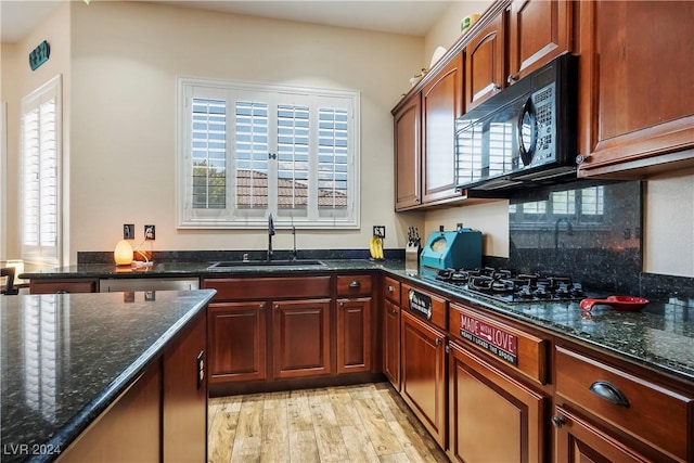 kitchen featuring light wood-style floors, dark stone countertops, a sink, black appliances, and backsplash