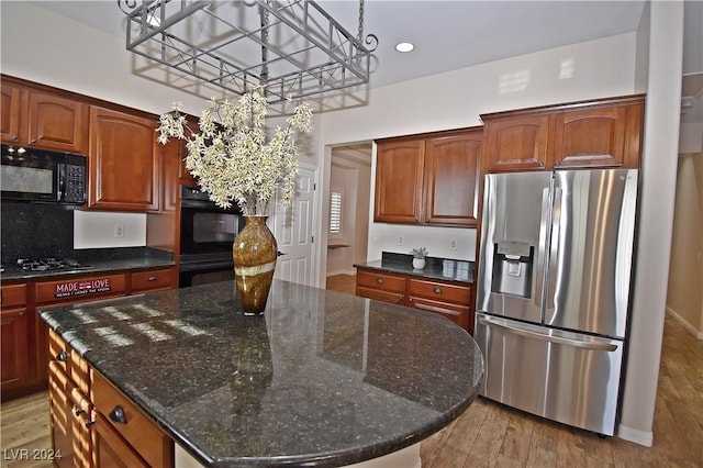 kitchen with dark stone countertops, a center island, light wood-style flooring, and black appliances