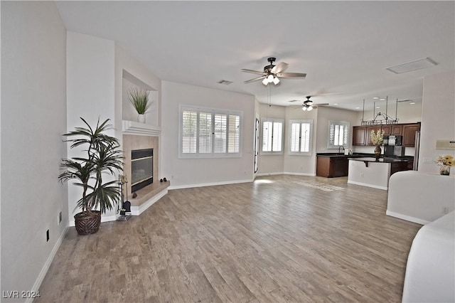 living room featuring a ceiling fan, visible vents, baseboards, light wood-type flooring, and a tiled fireplace