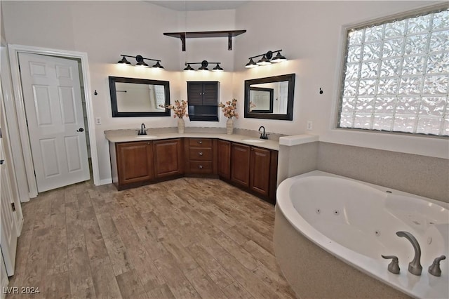 full bathroom featuring a jetted tub, double vanity, a sink, and wood finished floors