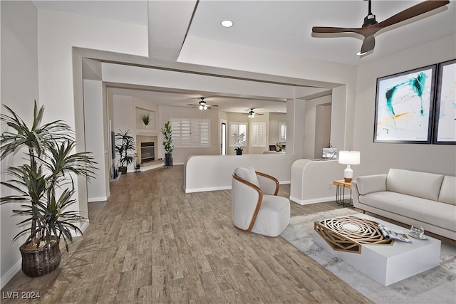 living area featuring baseboards, a ceiling fan, a glass covered fireplace, wood finished floors, and recessed lighting