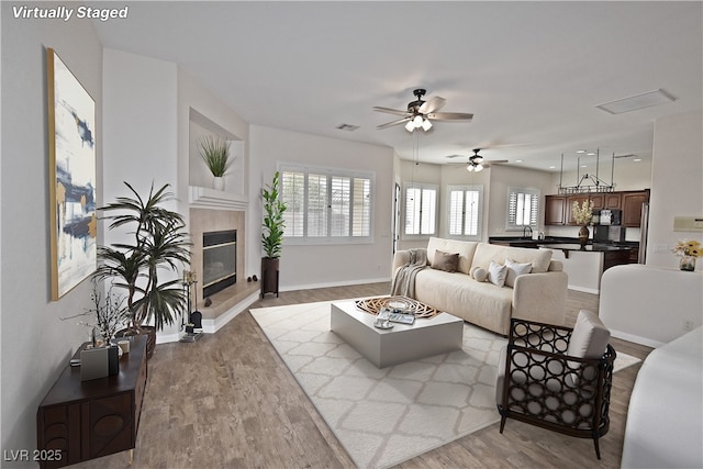 living room with a fireplace, light hardwood / wood-style floors, ceiling fan, and sink