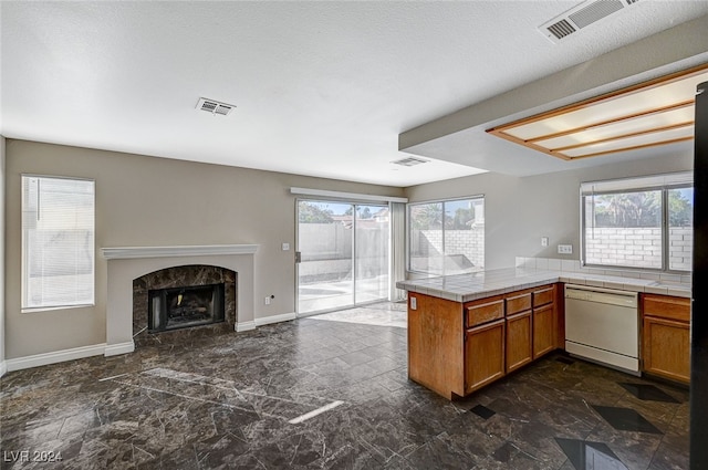 kitchen featuring white dishwasher, a textured ceiling, kitchen peninsula, and a high end fireplace