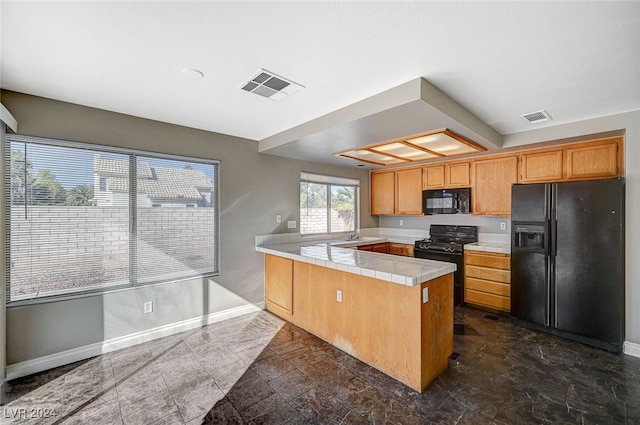 kitchen with black appliances, kitchen peninsula, and tile counters