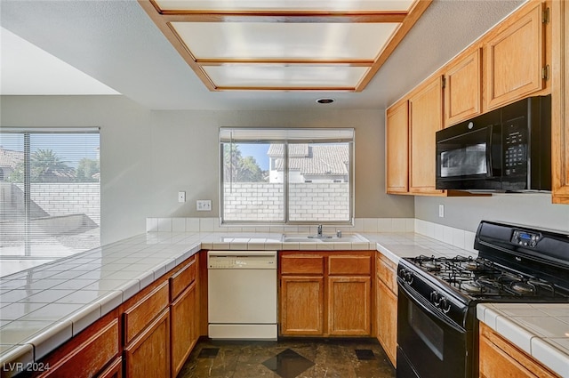 kitchen featuring tile countertops, black appliances, sink, and a wealth of natural light