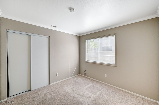 unfurnished bedroom featuring a closet, ornamental molding, and light colored carpet