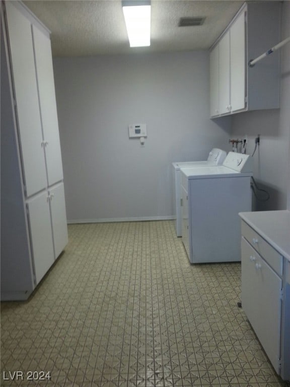 washroom with washing machine and clothes dryer, cabinets, and a textured ceiling