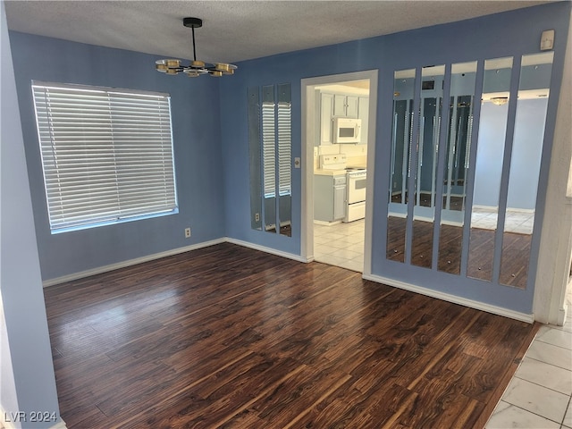 empty room featuring wood-type flooring, a textured ceiling, and a notable chandelier