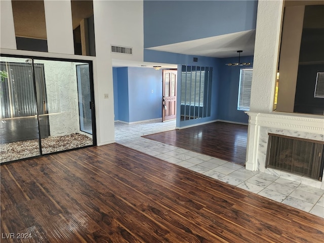 unfurnished living room with a high ceiling, light wood-type flooring, an inviting chandelier, and a premium fireplace