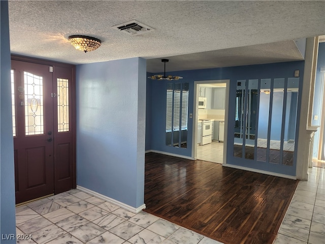 foyer entrance with an inviting chandelier, a textured ceiling, and light wood-type flooring