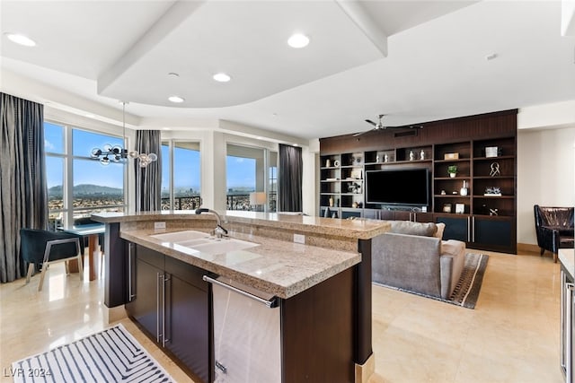 kitchen featuring sink, an island with sink, dark brown cabinets, pendant lighting, and light stone counters