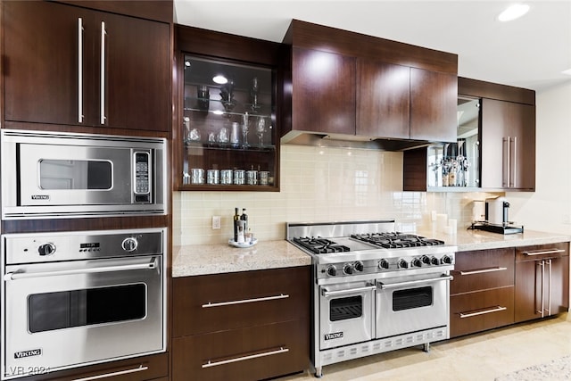 kitchen with backsplash, appliances with stainless steel finishes, light stone counters, and dark brown cabinets