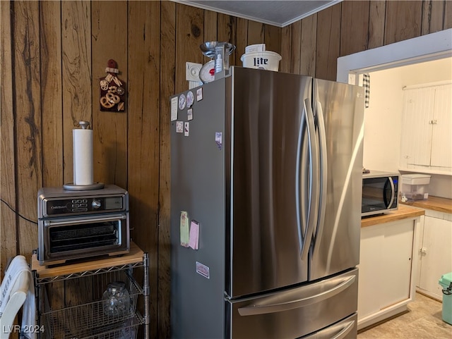 kitchen with wooden counters, wooden walls, stainless steel appliances, ornamental molding, and white cabinetry