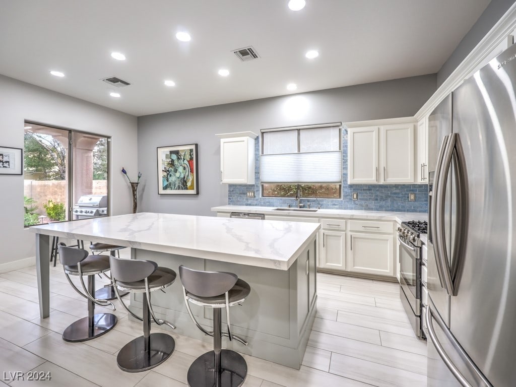 kitchen featuring stainless steel appliances, sink, a center island, white cabinetry, and light stone counters