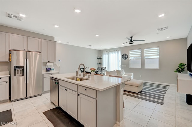 kitchen featuring appliances with stainless steel finishes, light tile patterned flooring, sink, light stone counters, and a kitchen island with sink