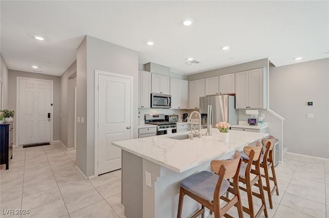 kitchen with a kitchen island with sink, a kitchen breakfast bar, stainless steel appliances, white cabinetry, and light stone counters