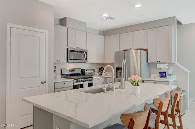 kitchen with light stone counters, stainless steel appliances, an island with sink, and white cabinets