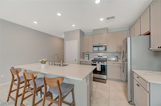 kitchen featuring sink, a kitchen island with sink, light stone counters, and stainless steel appliances