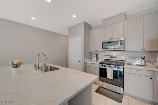 kitchen with appliances with stainless steel finishes, light stone countertops, a kitchen island with sink, light tile patterned flooring, and sink